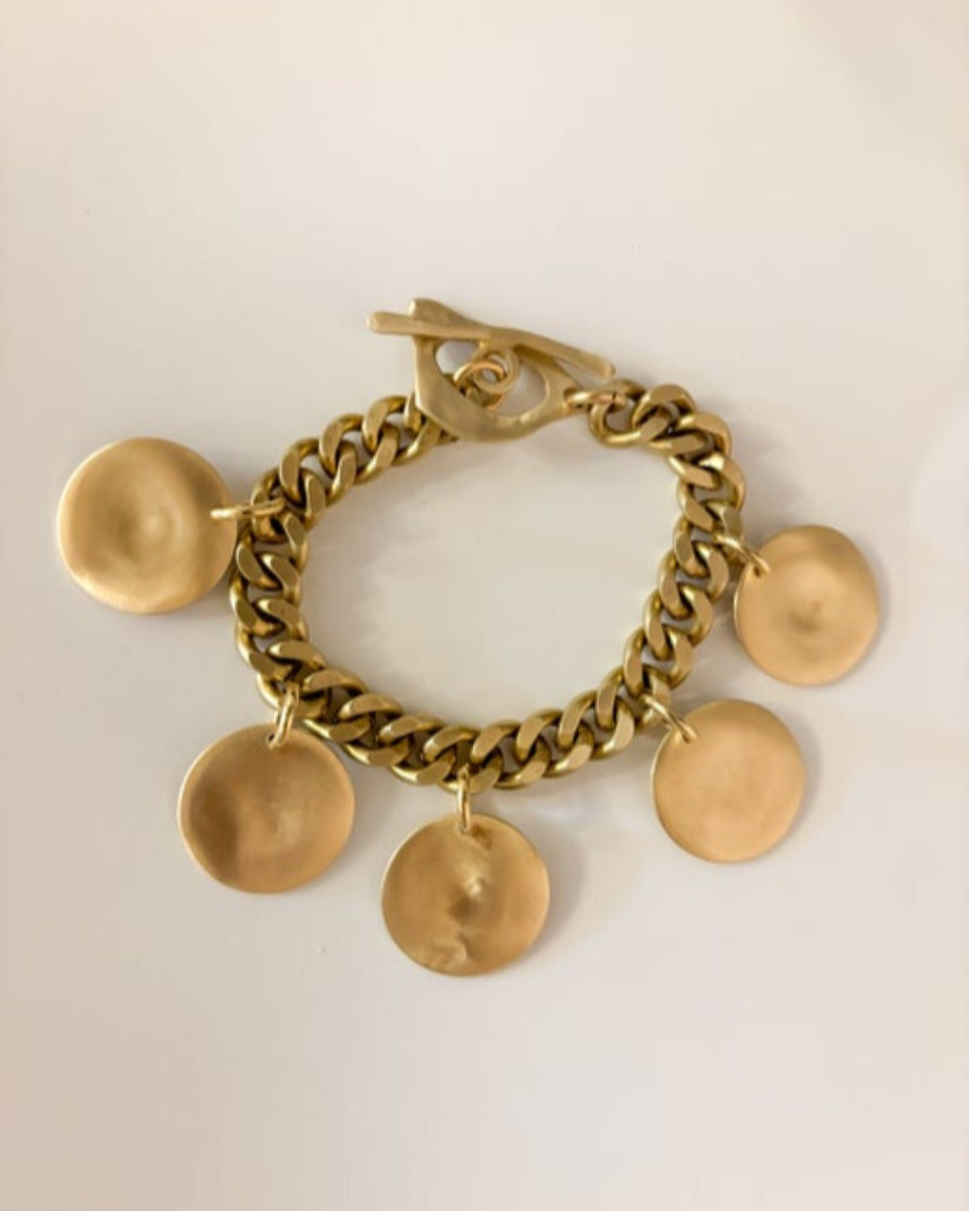 Gold chain bracelet with round pendants on a light beige background
