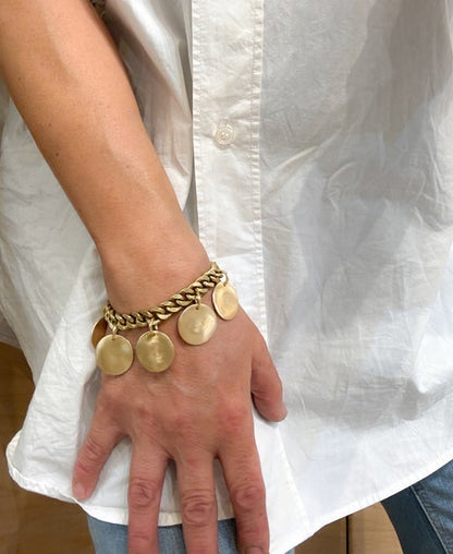 Gold bracelet with circular charms on a wrist against a white shirt background