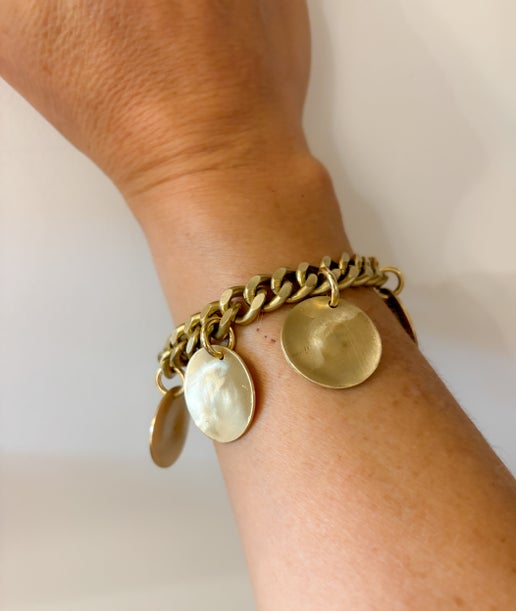 Gold chain bracelet with round pendants on a wrist against a light background