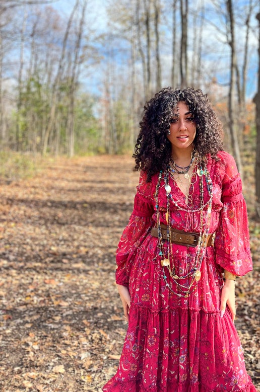Woman in a red dress standing in a forest wearing long beaded necklaces