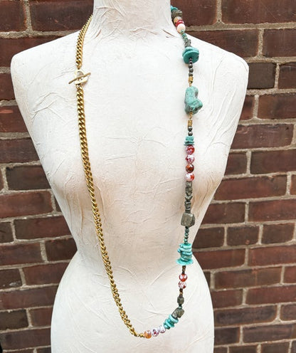 Necklace with colorful beads and gold chain on a mannequin against a brick wall.