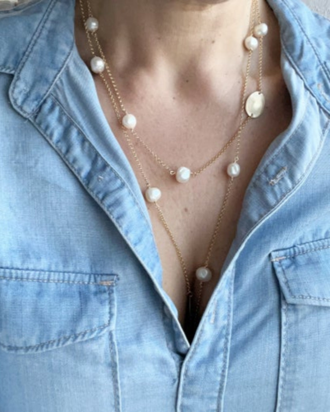 Long gold necklace with pearl detail worn by a person with a denim shirt