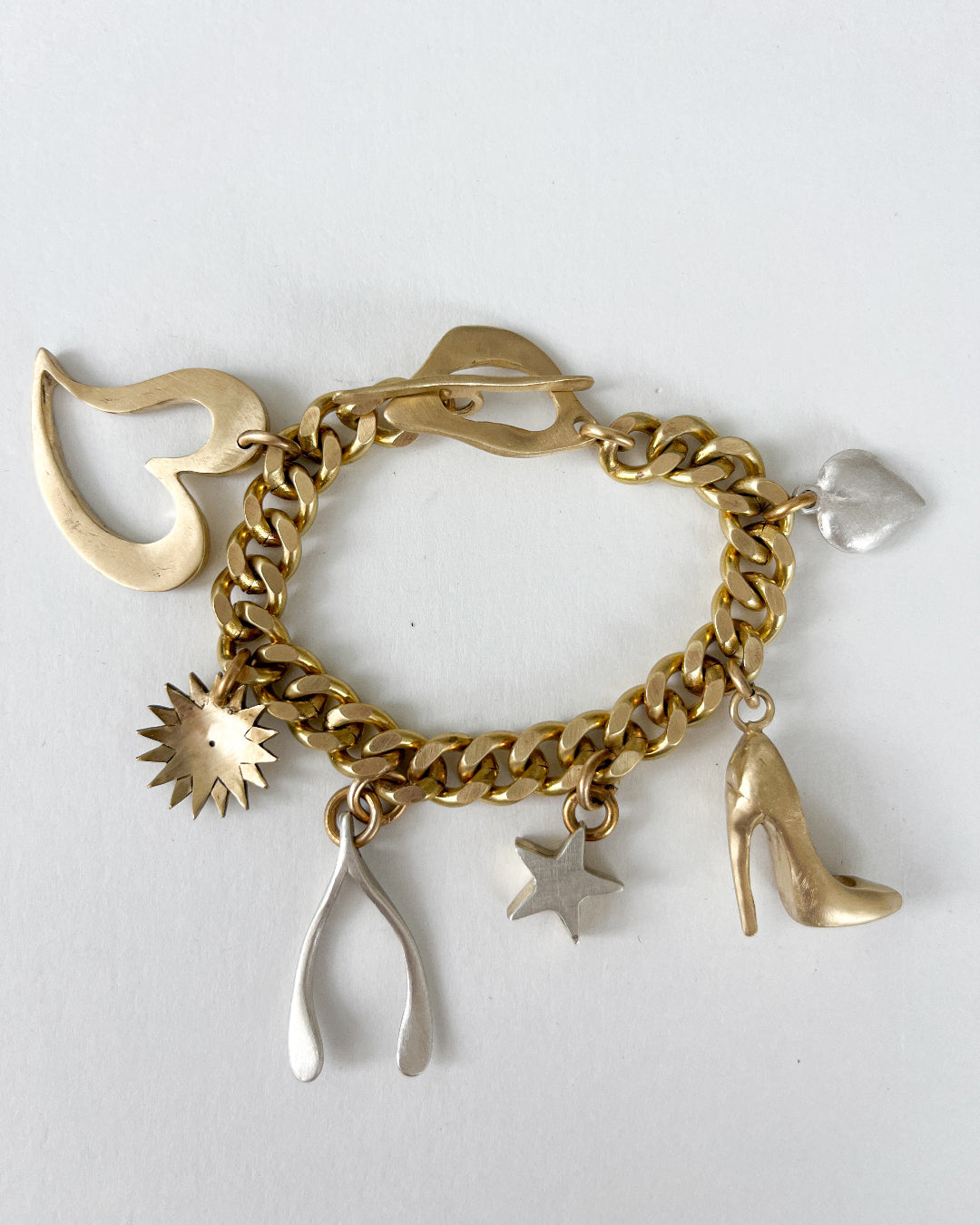 Gold chain bracelet with various bronze and silver charms on a white background