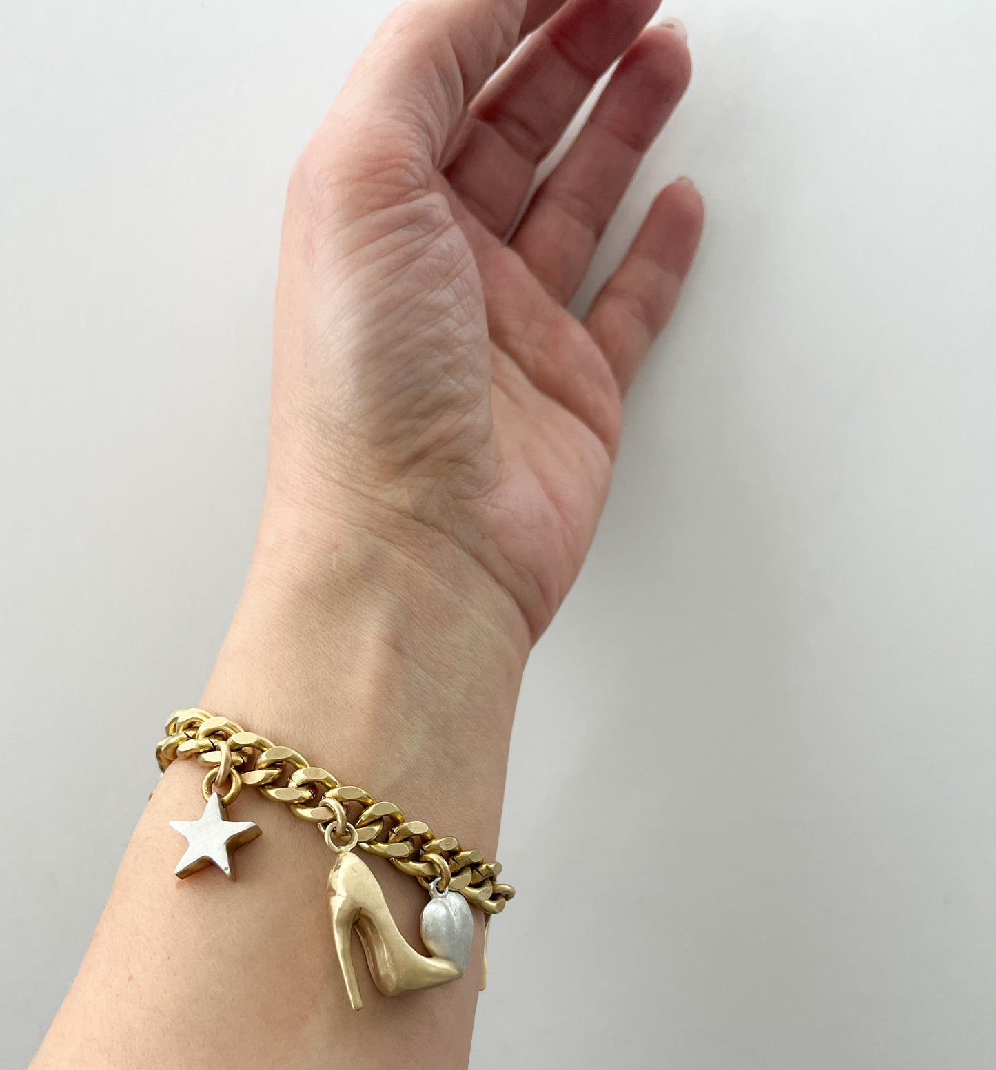 Gold bracelet with silver star and  gold high heel charm on a wrist against a light grey background