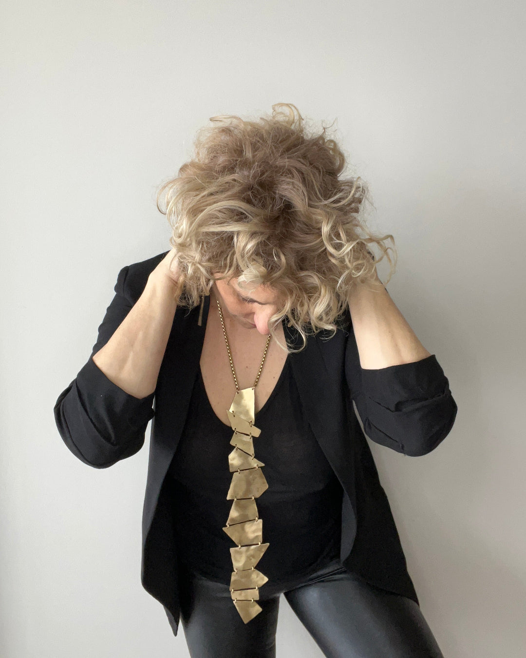 Person wearing a black outfit with a long, gold necklace against a plain background