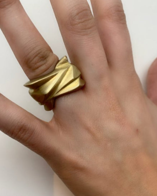 Gold textured ring on a finger against a white background