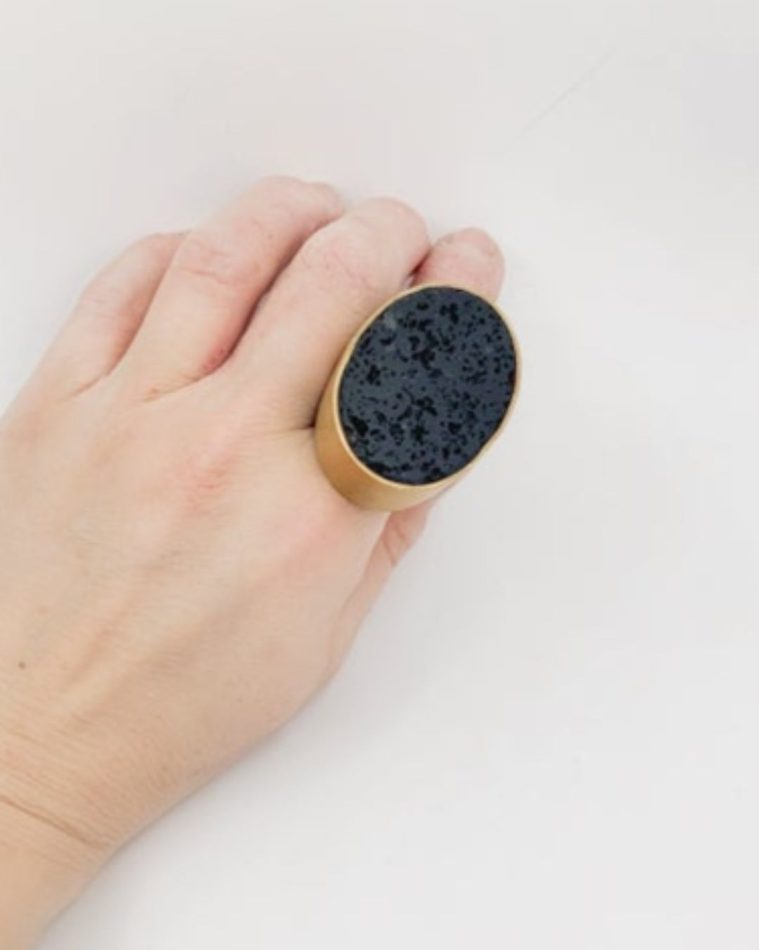Hand wearing a bronze ring with an oval black stone on a white background