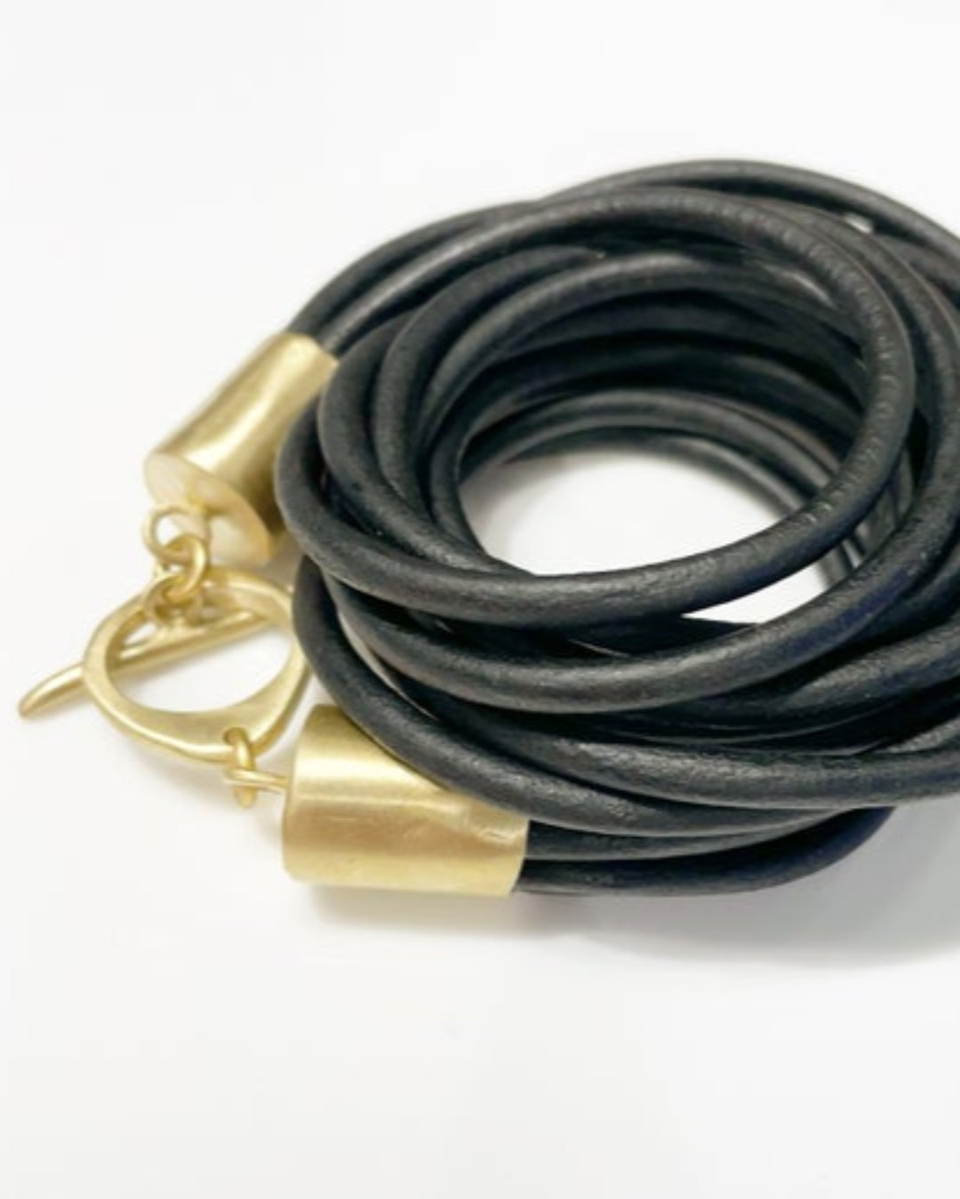 Multi-strand black leather bracelet with gold metal details on a white background