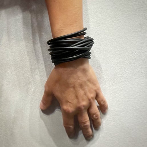 Hand wearing a black multi-strand leather bracelet on a light gray background