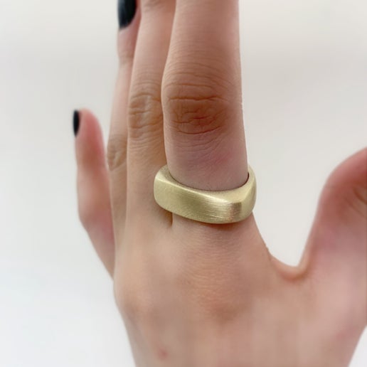 Geometric gold ring on a person's finger against a white background