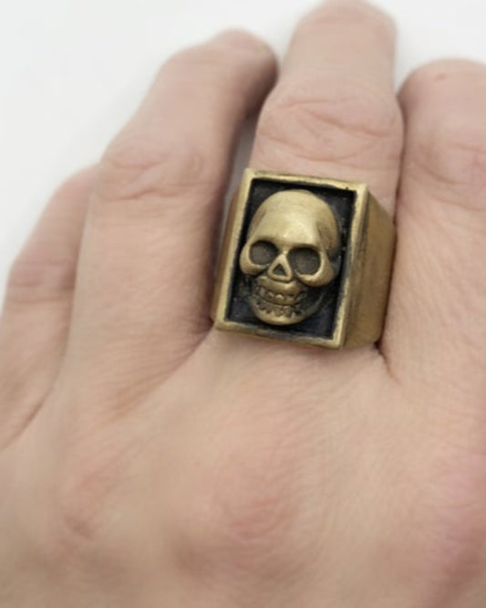 Gold ring with skull detail on a hand against a white background