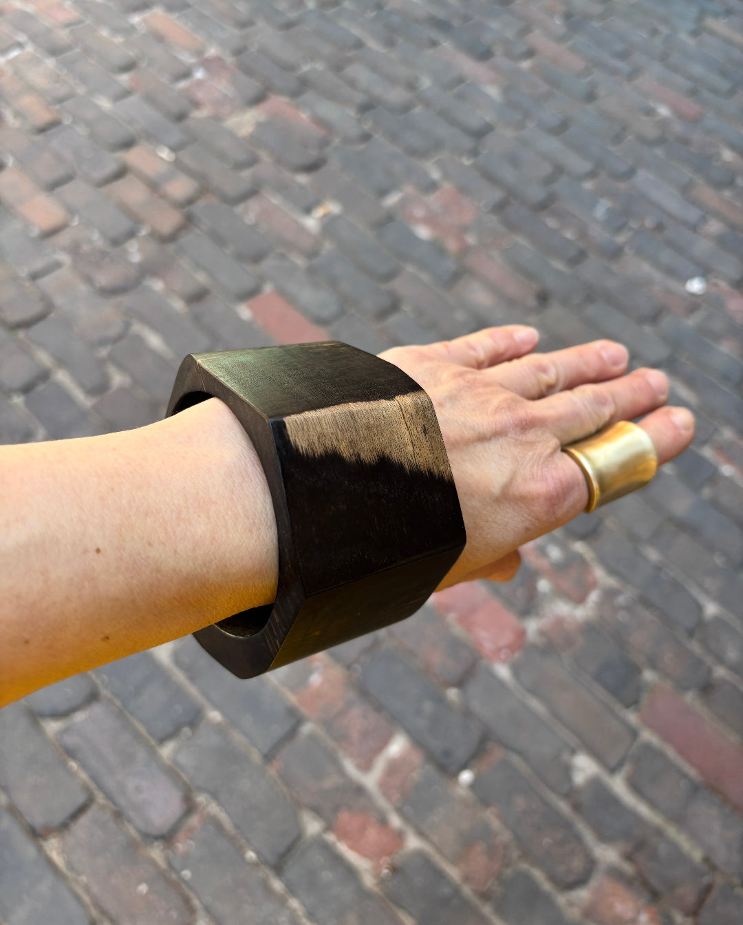 Hand wearing an ebony bracelet on a brick pavement background
