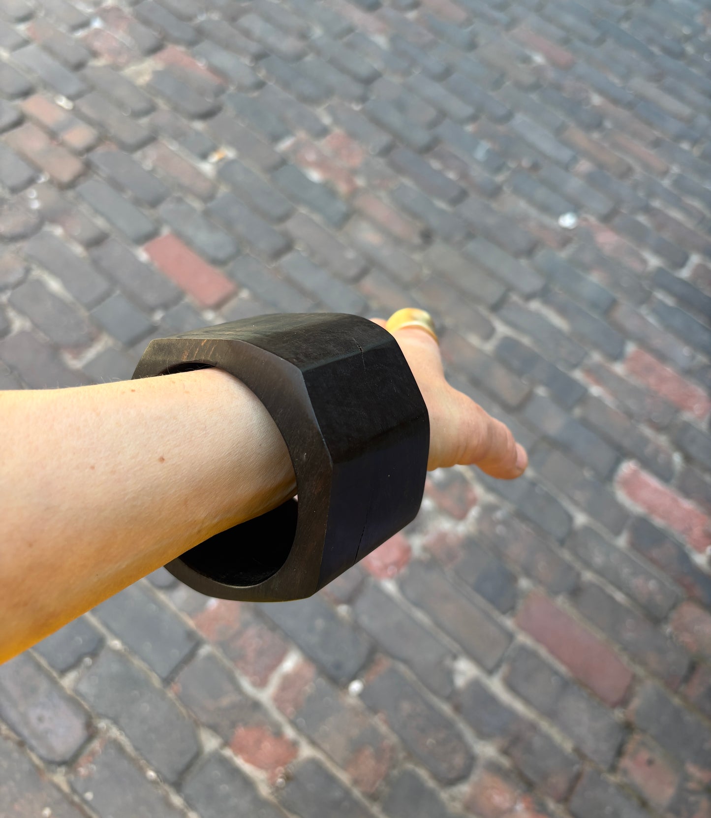 Ebony bracelet on a person's wrist with a blurred cobblestone street background