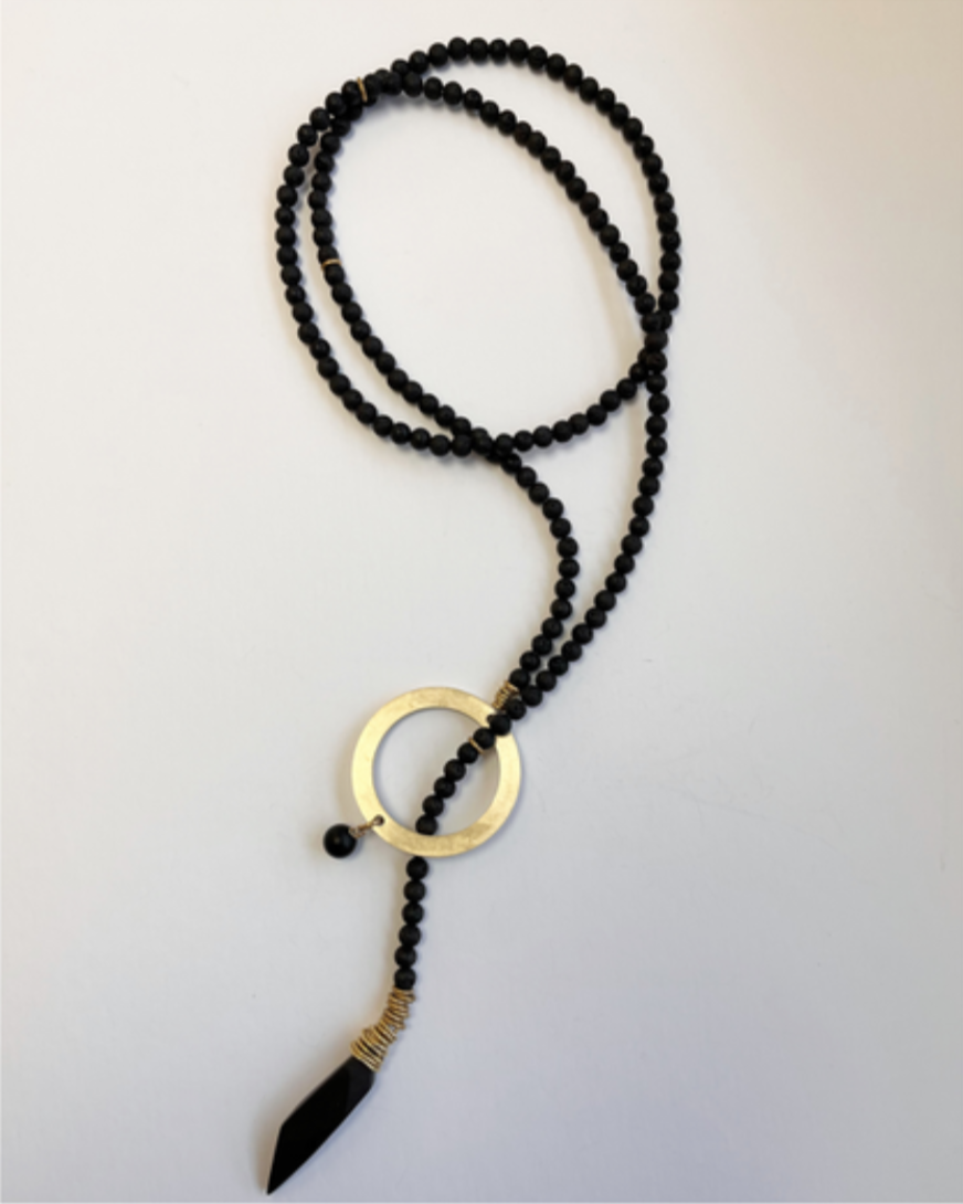 Black beaded necklace with a gold pendant on a light gray background