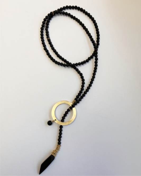 Black beaded necklace with a gold pendant on a light gray background
