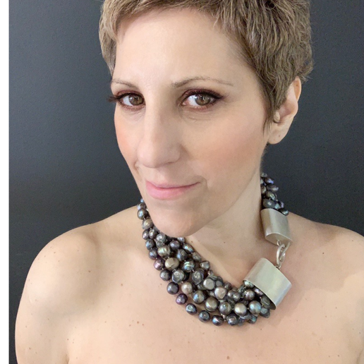 Woman wearing a layered dark grey pearl necklace with a dark background