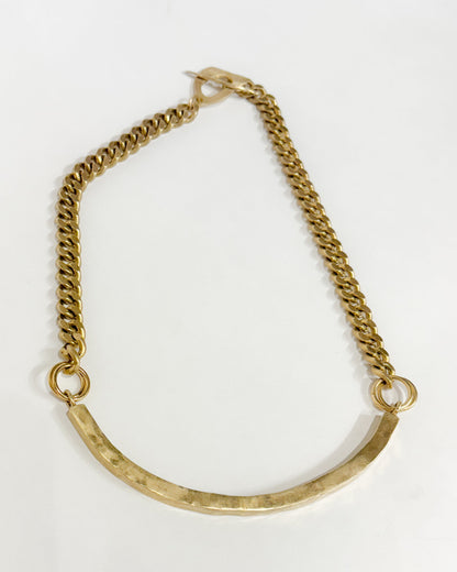 Gold necklace wiith a curved design on a white background