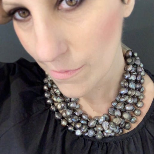 Close-up of a person wearing a layered dark grey necklace with a black top against a dark background