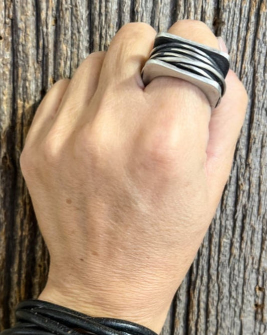 Hand wearing a silver ring with wire detailing  against a wooden background