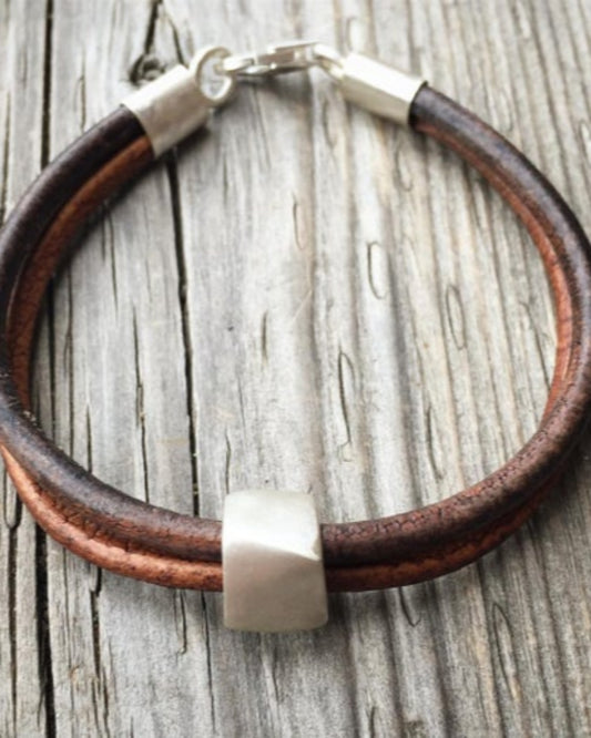 Brown leather bracelet with silver clasp on a wooden surface