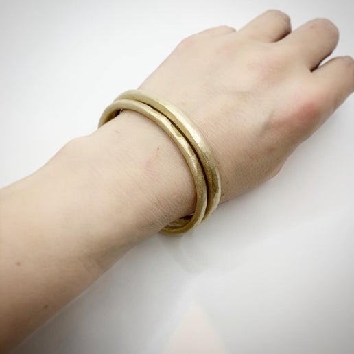 Hand wearing two solid metal bangles on a light background