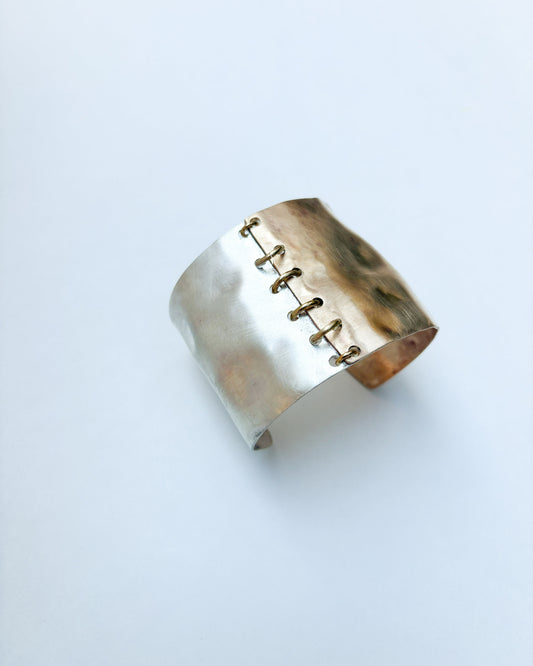 Silver and gold cuff bracelet on a light gray background