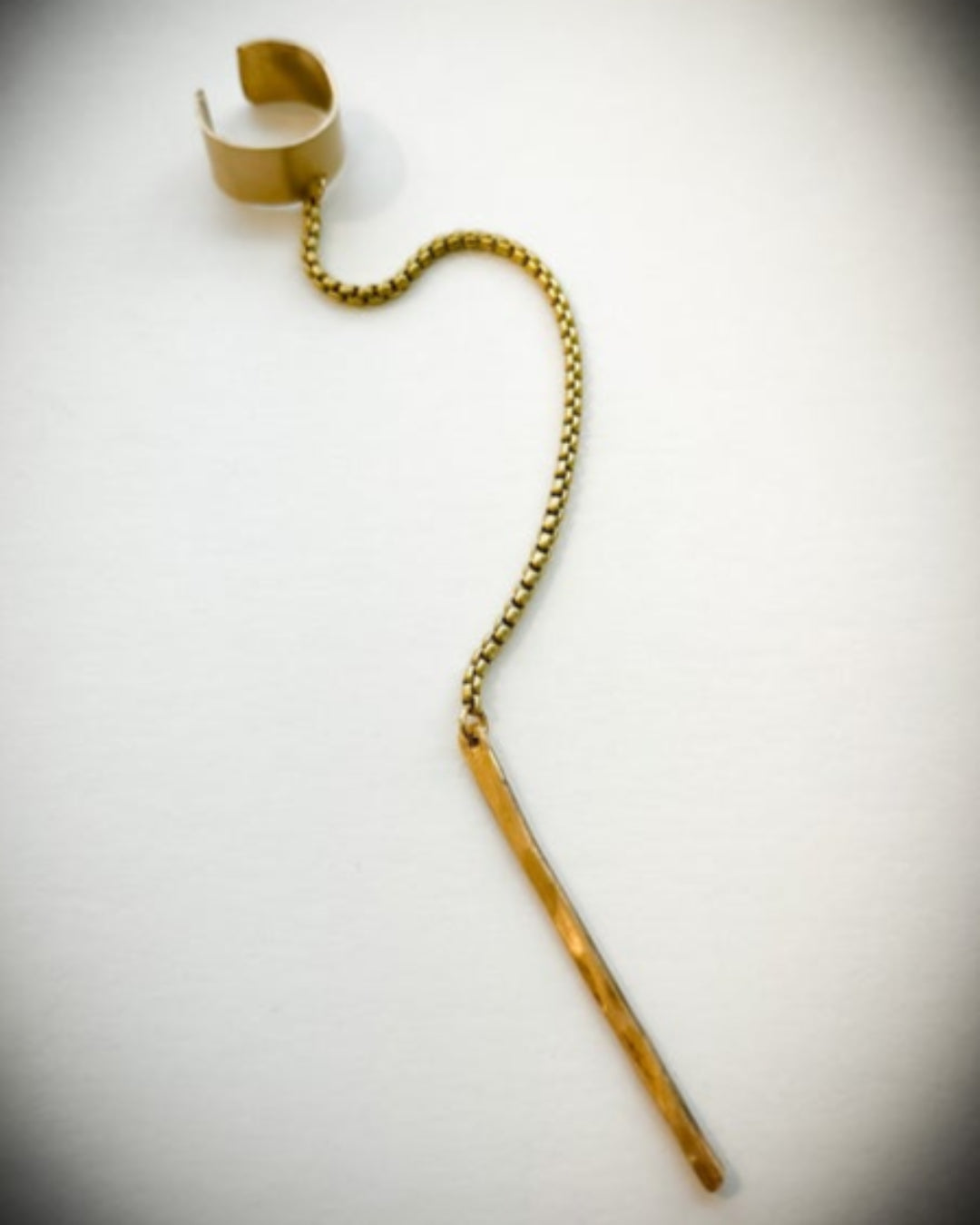 Gold-coloured ear cuff with a chain and metal bar detail on a white background