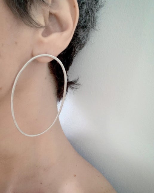 Close-up of a person wearing a large silver hoop earring with a neutral background