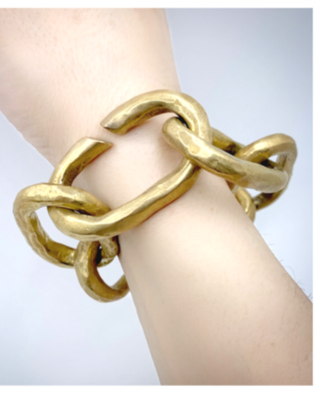Gold chain bracelet on a wrist against a light background