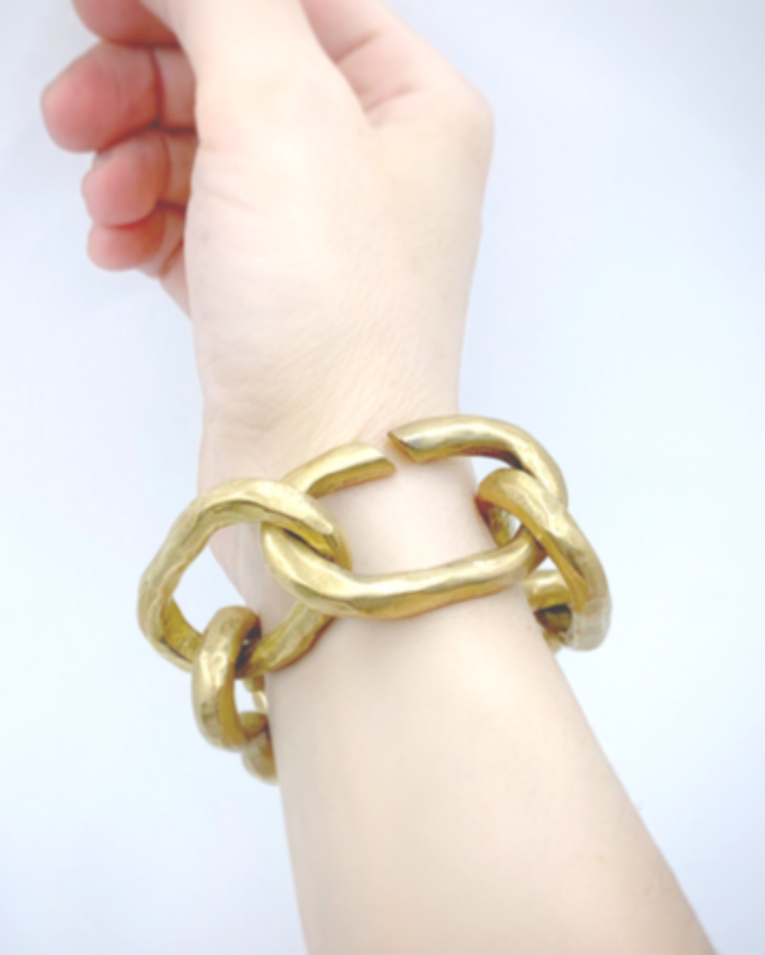 Gold chain bracelet on a wrist against a light blue background