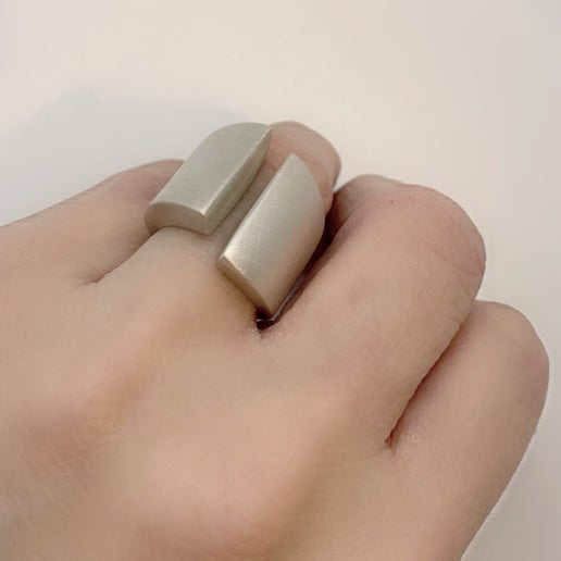 Hand wearing a silver ring with a geometric design on a plain background