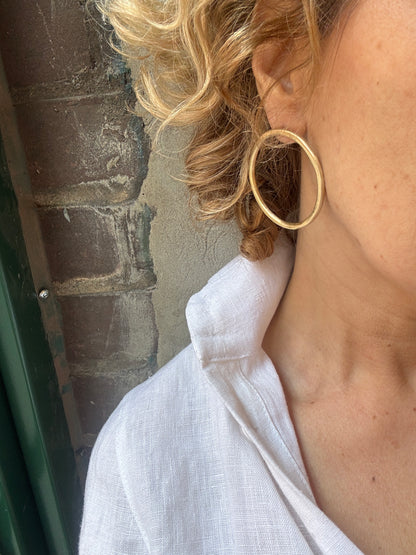 Close-up of a person with blonde hair and a white shirt wearing a gold hoop earrings standing against a brick wall. 