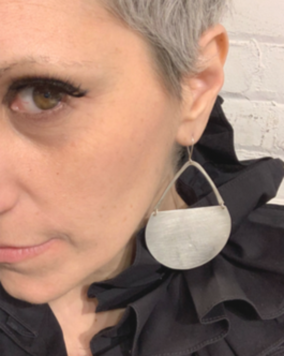 Person wearing a large silver earring with a plain background
