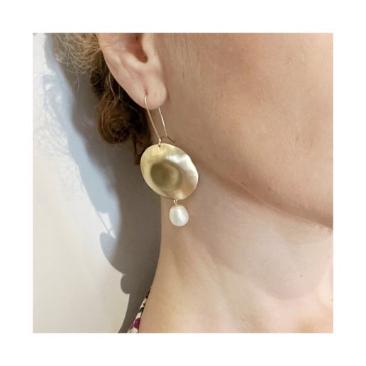 Person wearing a gold earring with a dangling pearl on a white background