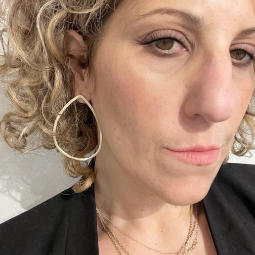 Close-up of a woman wearing gold  teardrop hoop earrings and a black top against a white background