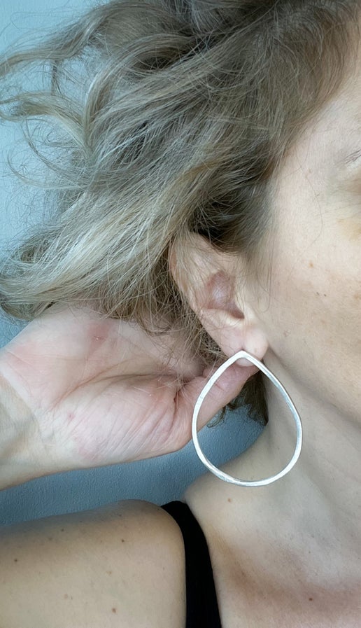 Close-up of an ear with a silver teardrop hoop earring against a neutral background