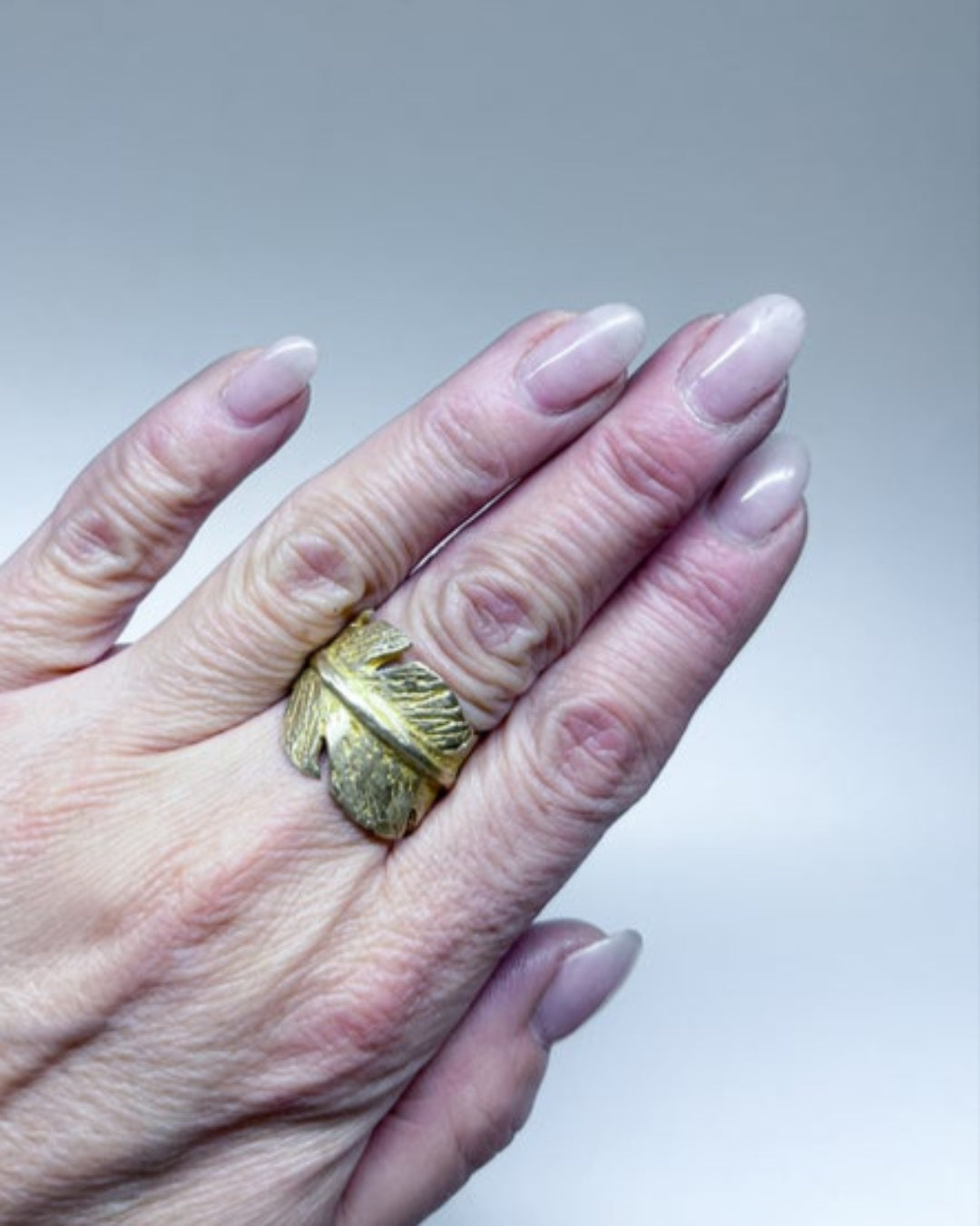 Hand wearing a bronze ring with feather detail on a neutral background