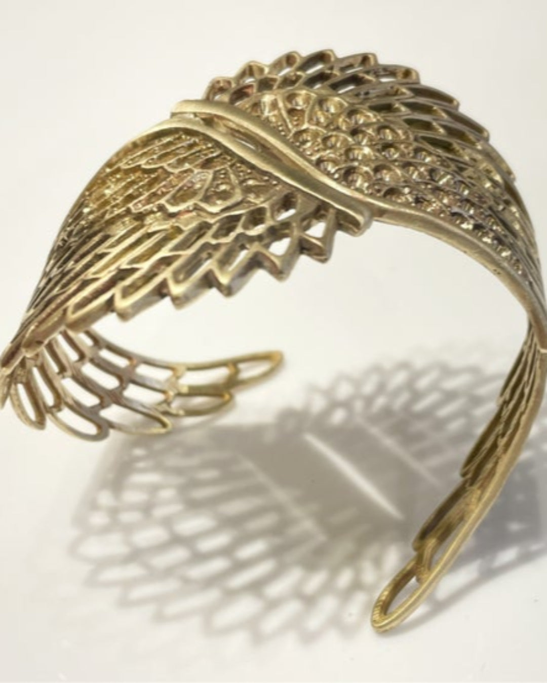 Gold cuff with wing detailing on a light background