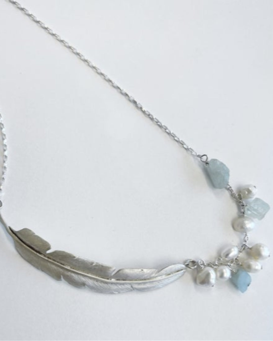 Silver necklace with feather design and blue crystals on a white background