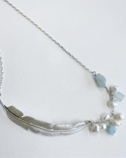 Silver necklace with feather design and blue crystals on a white background