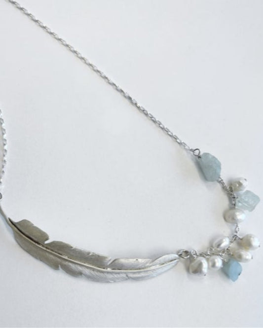 Silver necklace with feather design and blue crystals on a white background