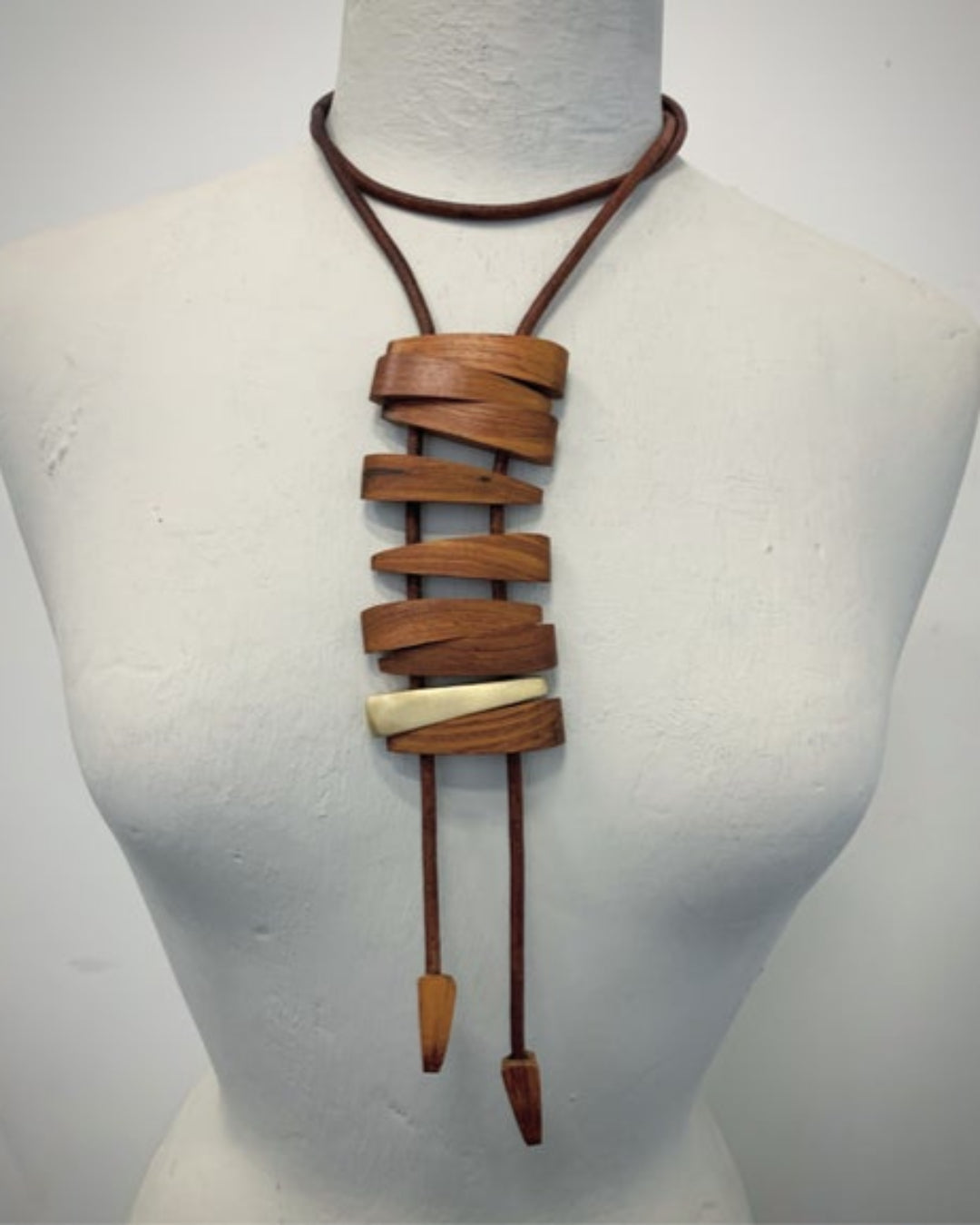 Brown leather cord necklace with brown wood and bronze details  on a mannequin against a white background