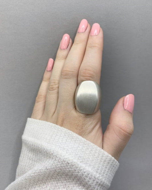 Hand wearing a large silver ring with pink nail polish against a grey background