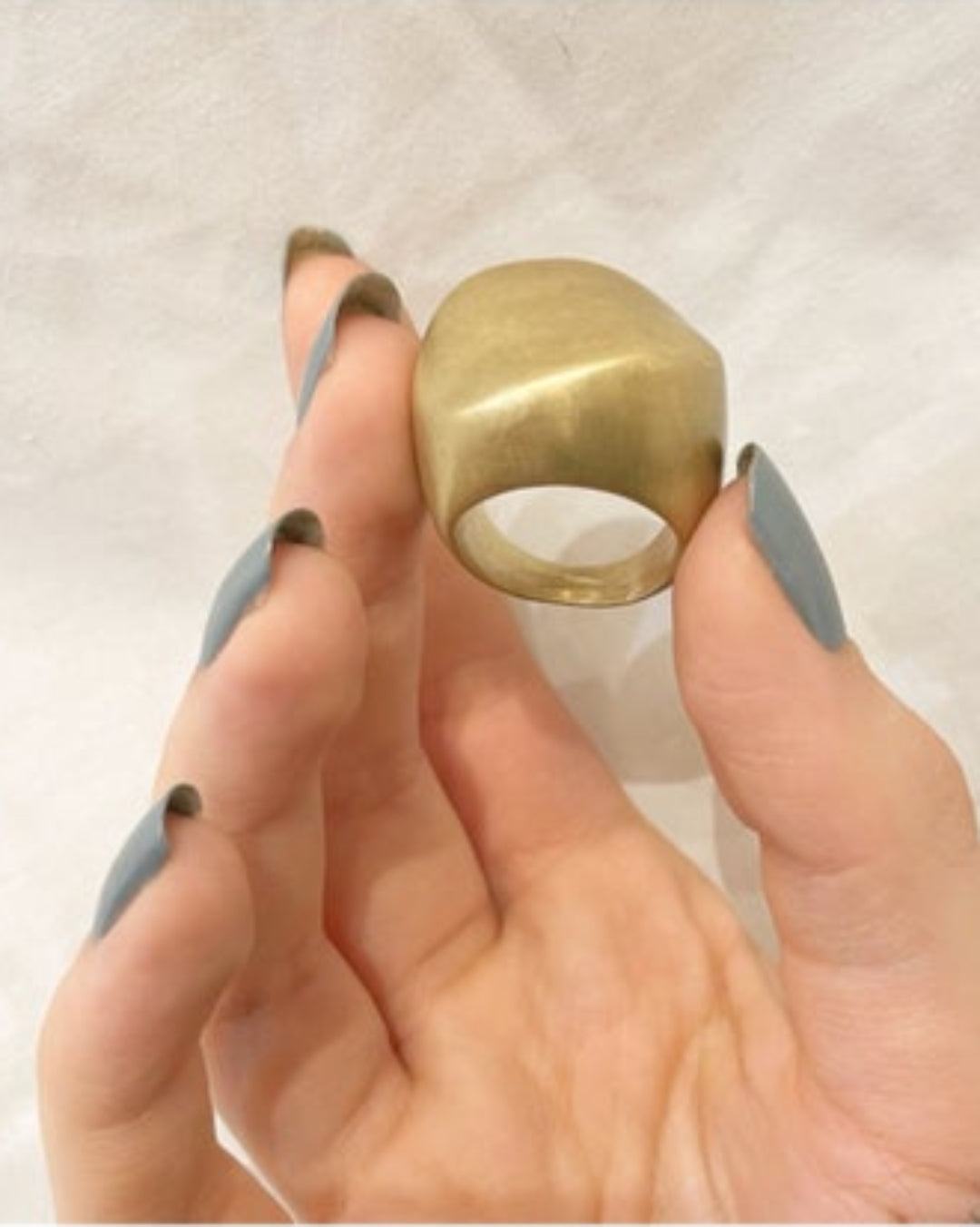 Chunky gold ring being held between fingers with a neutral background