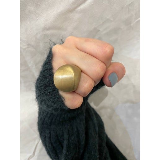 Hand wearing a large gold ring on a neutral background