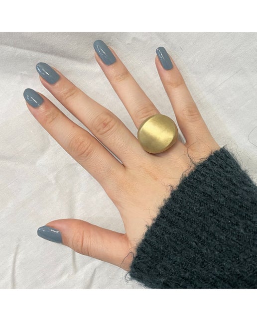Hand wearing a gold ring with gray nail polish on a white background