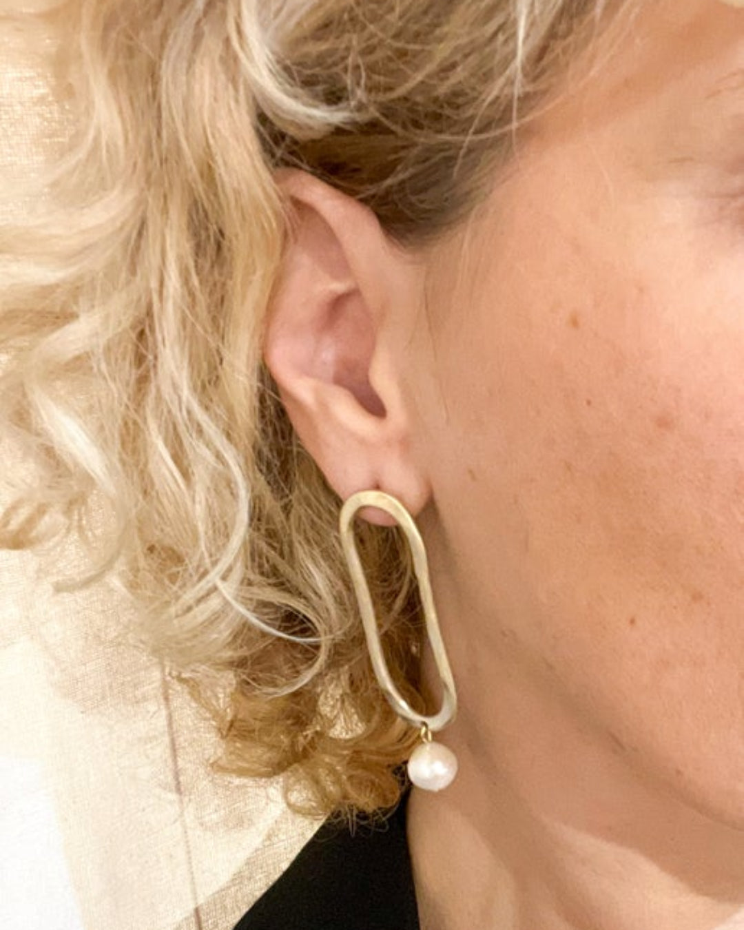Close-up of a person wearing a gold hoop earring with a pearl accent.