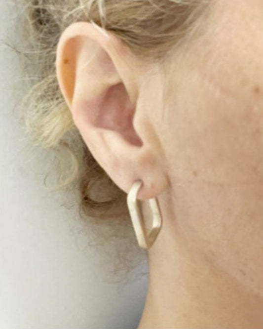 Close-up of a person wearing a gold hoop earring with a neutral background