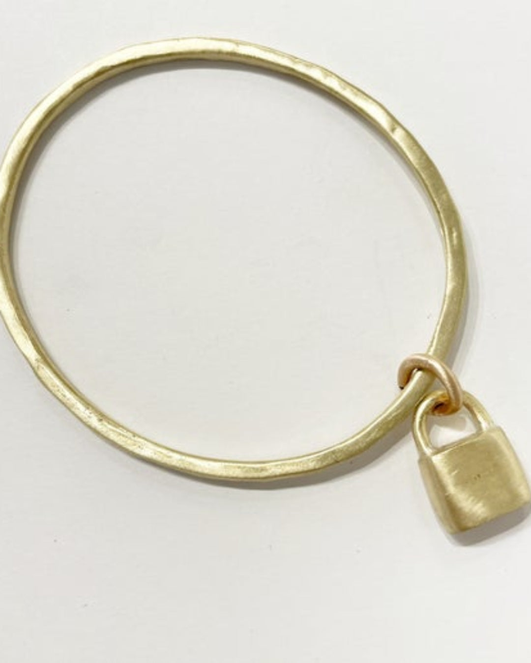 Gold bangle with a lock charm on a light grey background