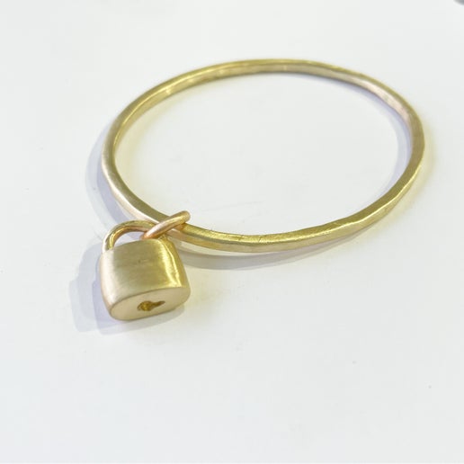 Gold bangle with a small padlock charm on a white background